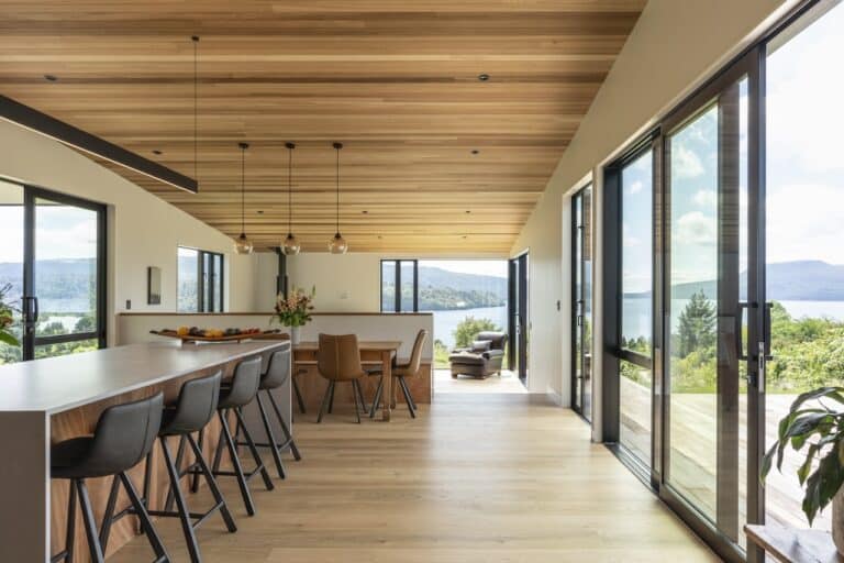 Light coloured natural wood flooring in open kitchen dining lounge space with timber ceiling