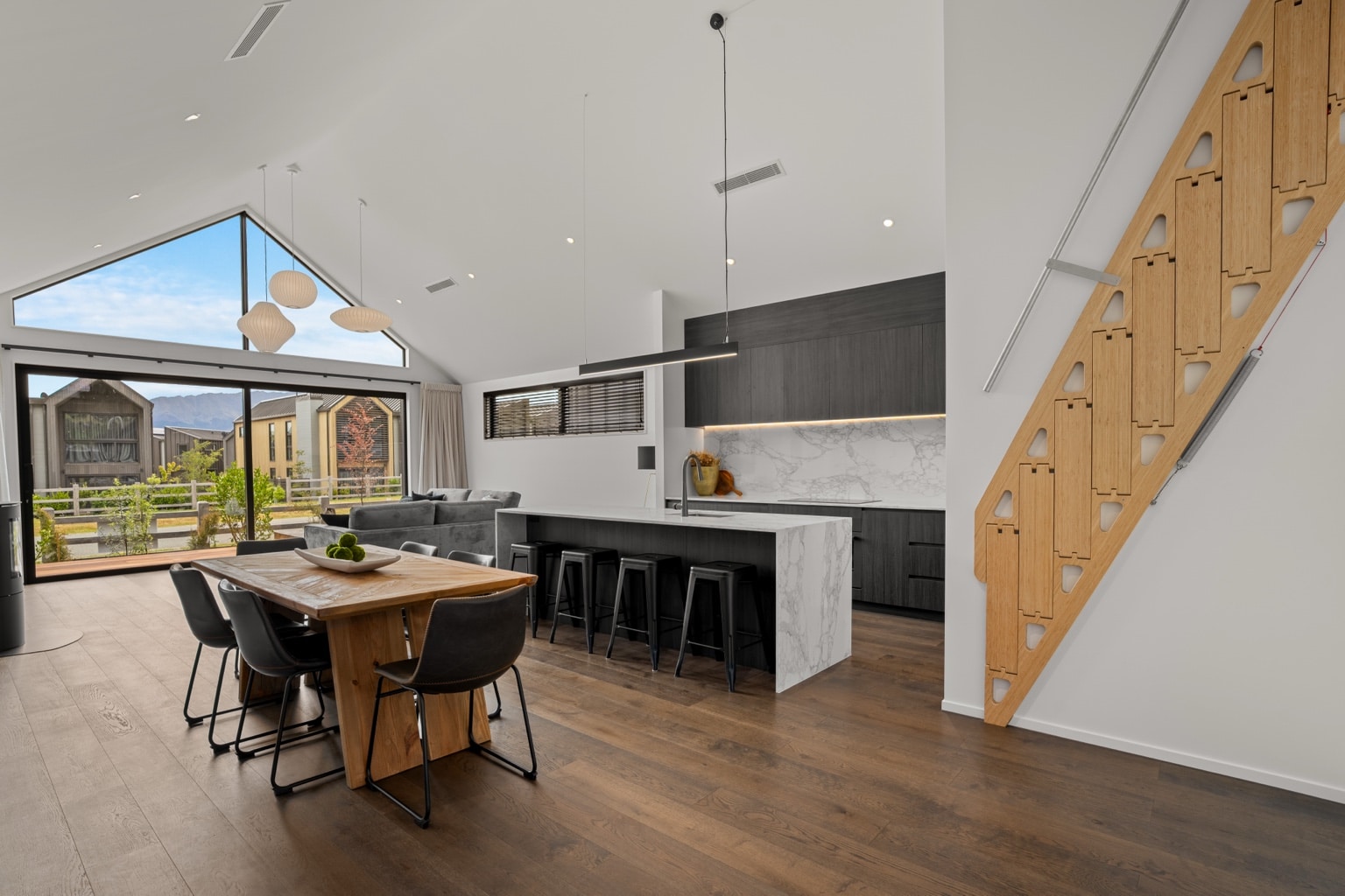 Wide plank European oak flooring in a modern kitchen with marble island, timber dining table and architectural loft staircase in a Queenstown New Zealand home