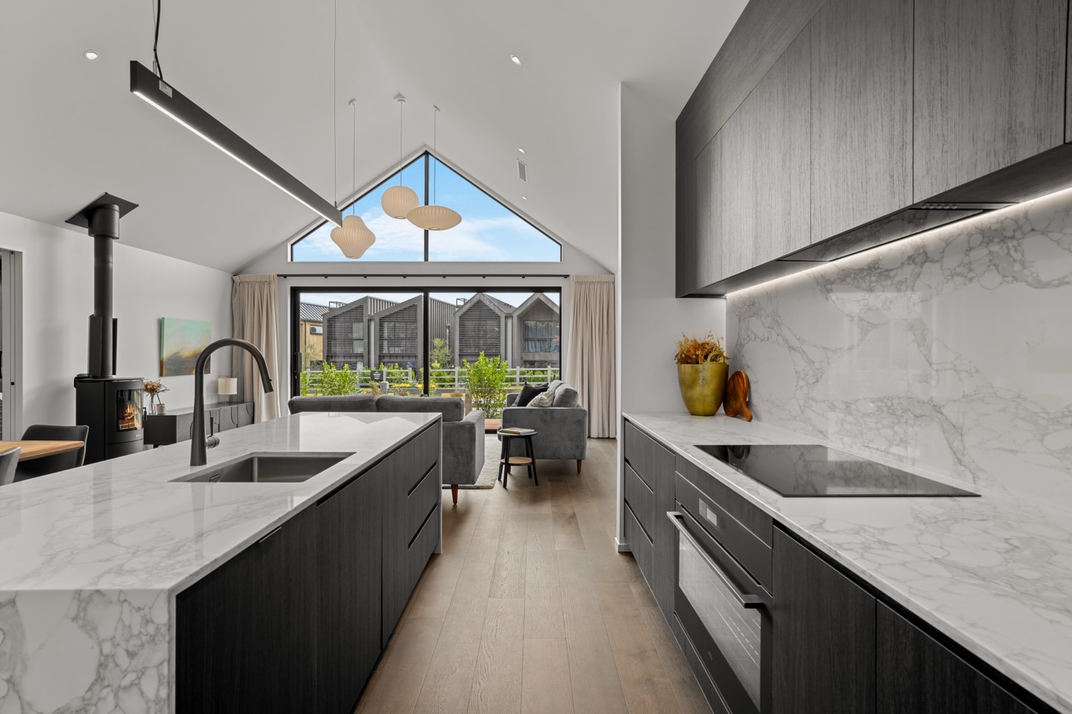 Wide plank European oak flooring in a modern kitchen and living room with marble island bench and large gable window bringing natural light into a Queenstown New Zealand home