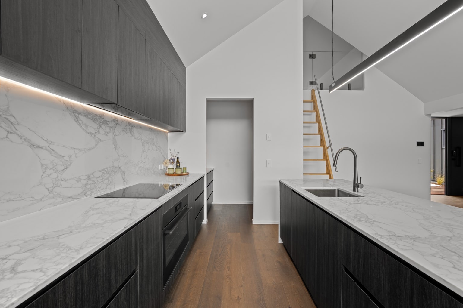 Wide plank European oak flooring in a modern kitchen with marble island bench, dark timber cabinetry and loft staircase in a Queenstown New Zealand home