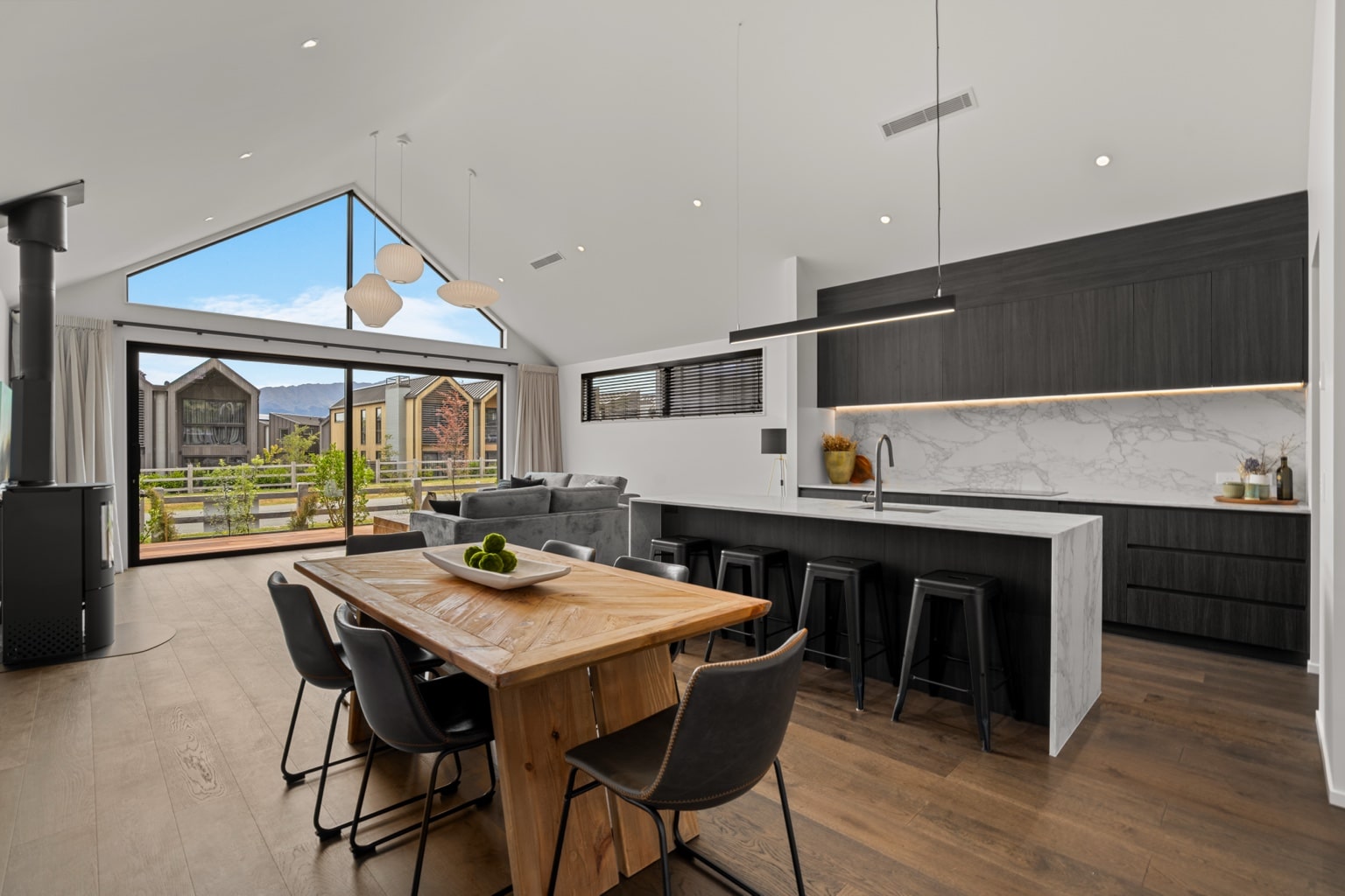 Wide plank European oak flooring in an open plan kitchen and living area with marble island, dining table and mountain view windows in a Queenstown New Zealand home