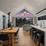 Wide plank European oak flooring in an open plan kitchen, dining and living area with marble island and gable window at twilight in a Queenstown New Zealand home