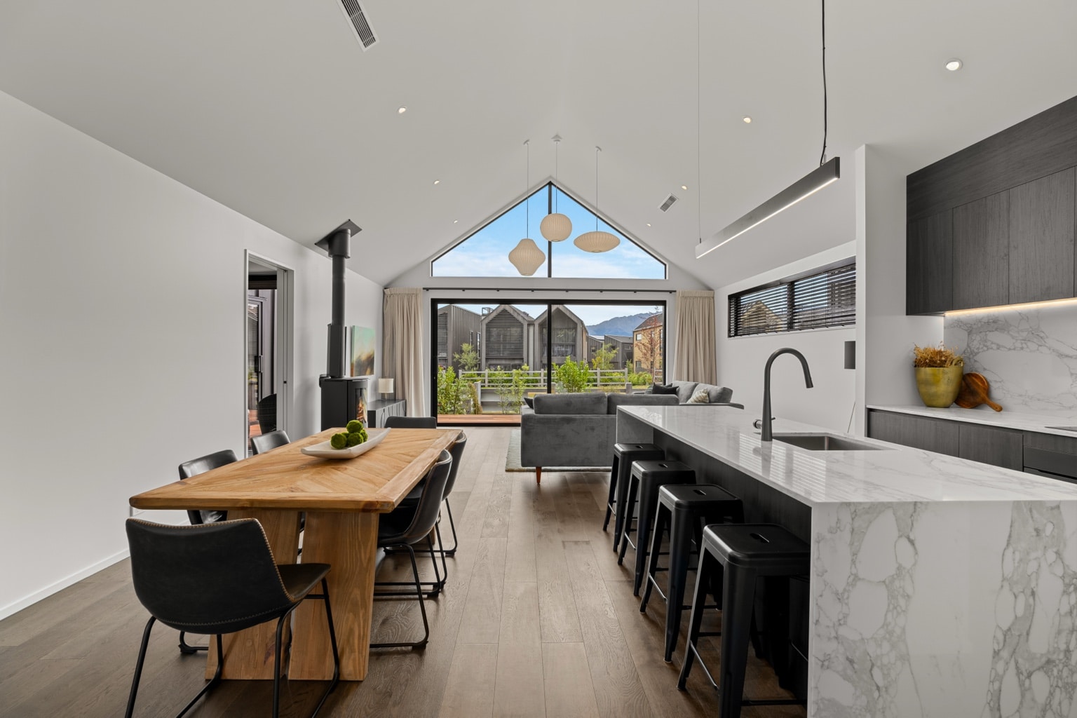 Wide plank European oak flooring running through a modern open plan kitchen, dining and living interior with large gable window in a Queenstown New Zealand home