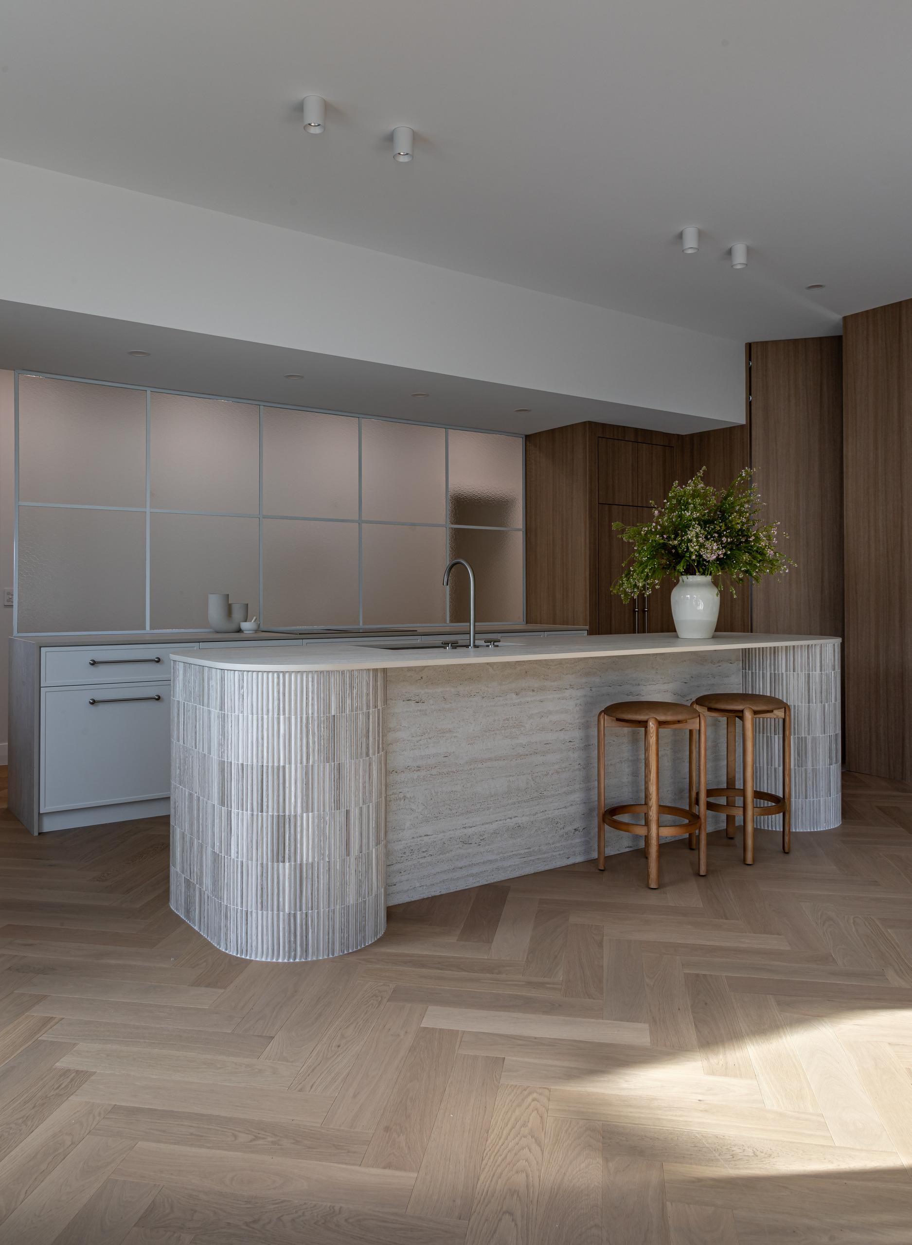 Curved fluted-tile kitchen island and warm oak joinery above Bordeaux Herringbone parquet in a Ponsonby home.