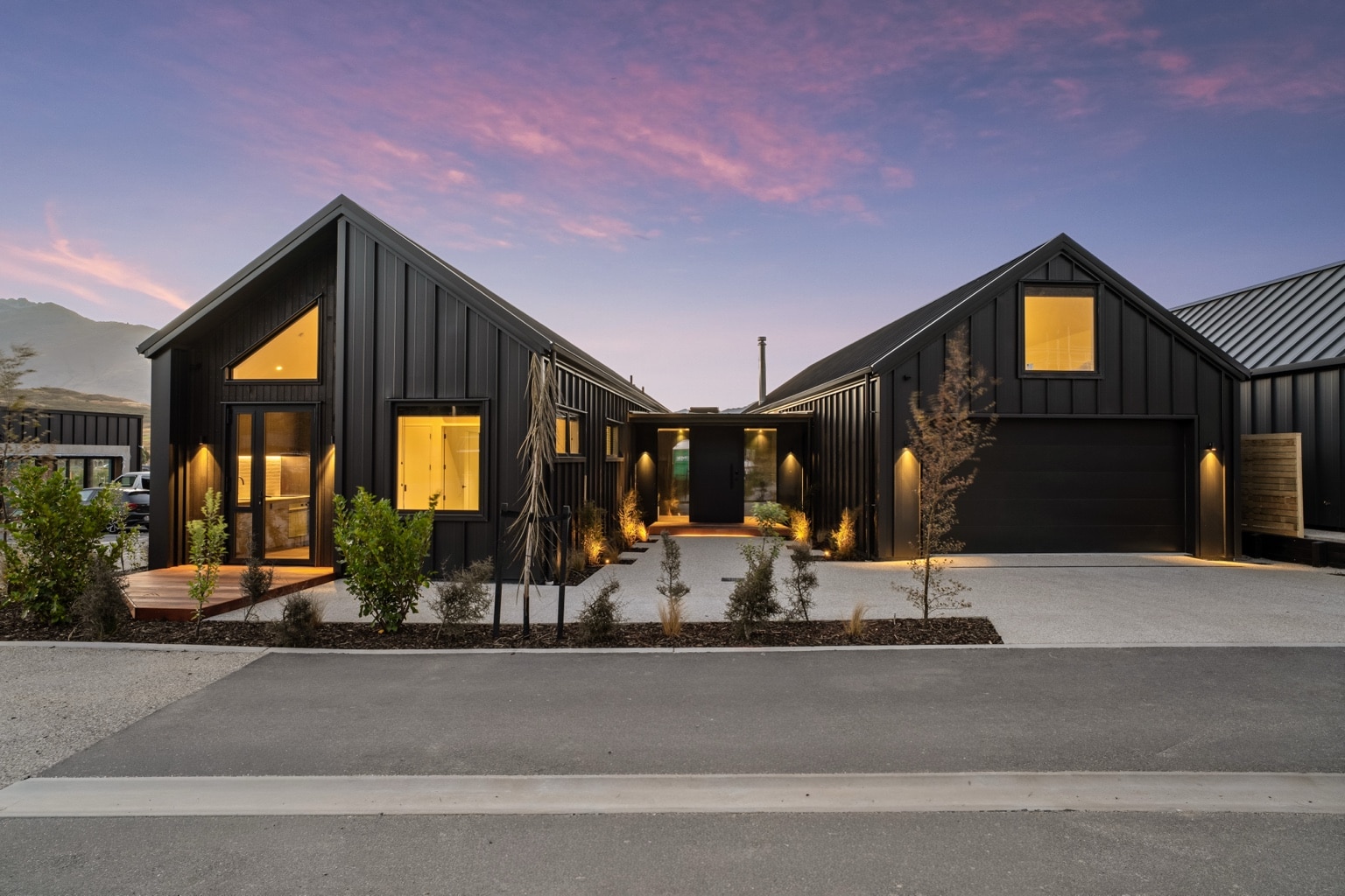 A black-clad gabled Jacks Point home glowing at twilight, Queenstown.
