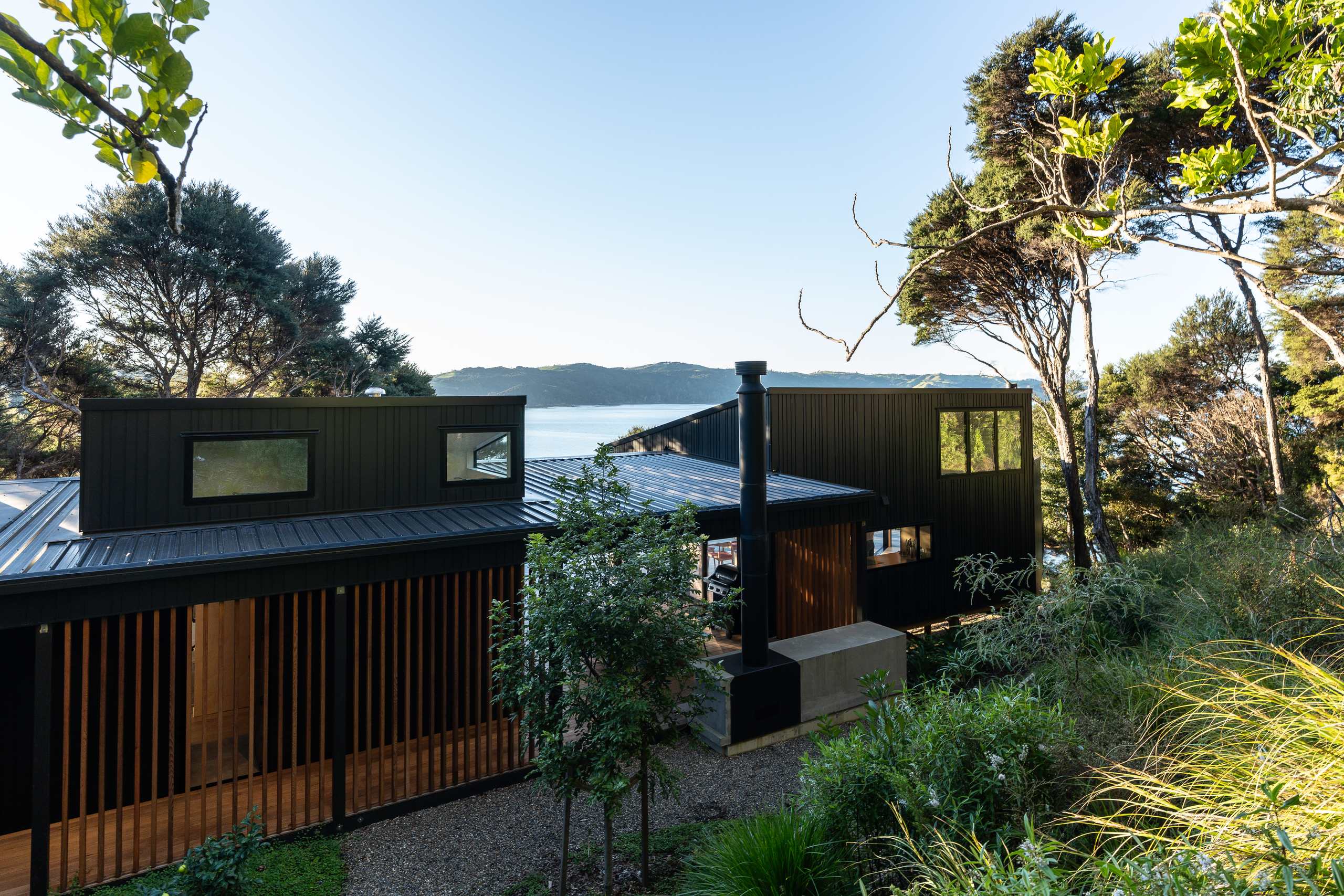 A dark-clad Waiheke Island home built by Box Build, set into bush above the Hauraki Gulf.