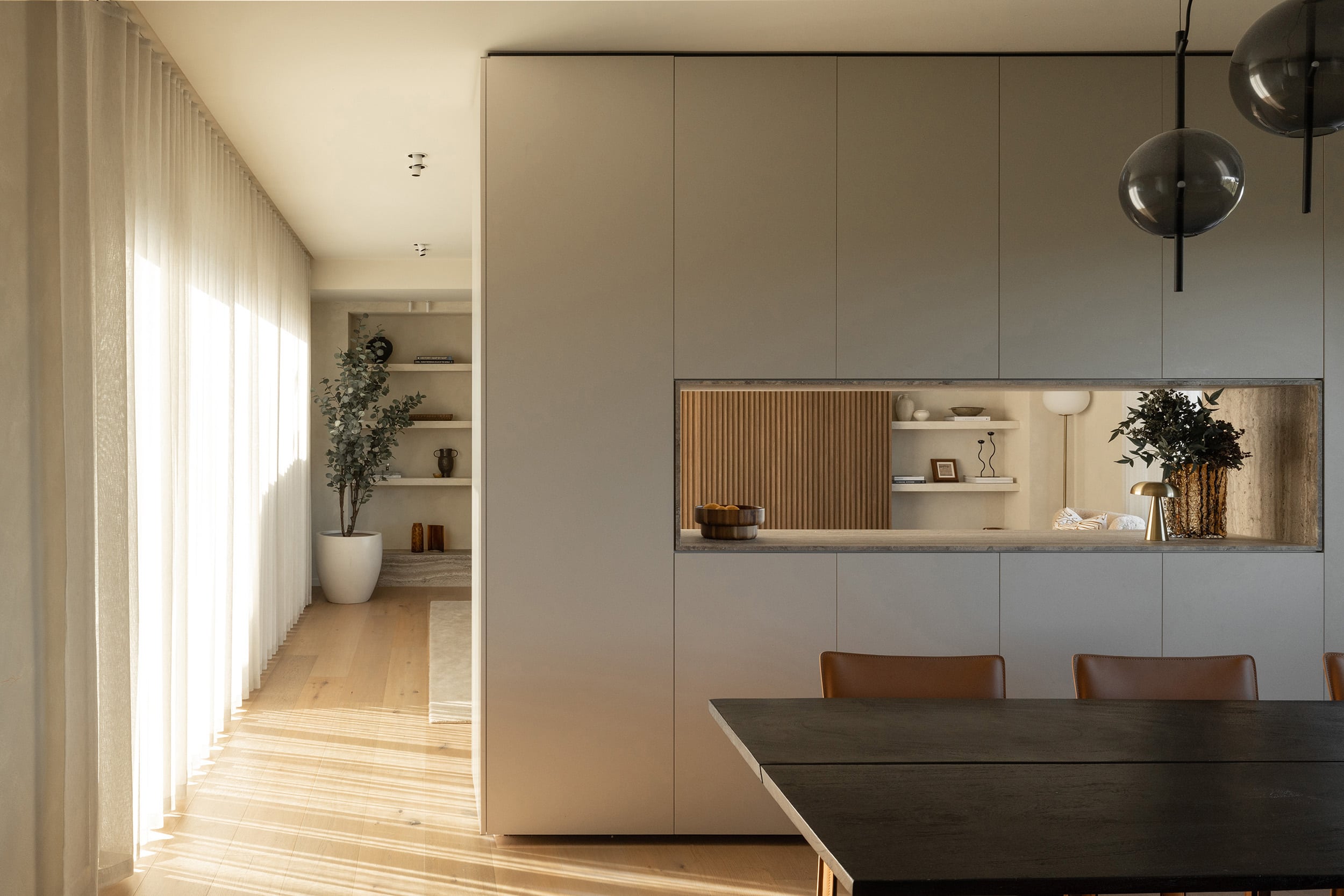 Icons Conde oak flooring in an open dining room, with a pale joinery wall, a lit display niche and a dark timber table.