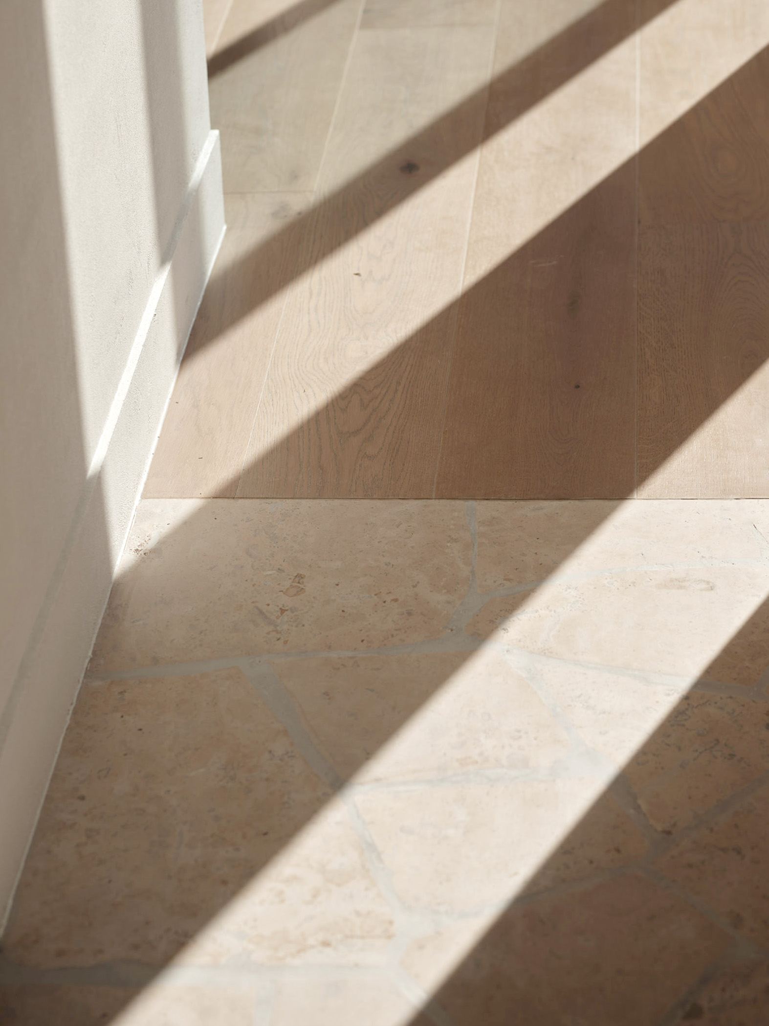 Close view of Icons Conde oak flooring meeting a stone-tiled threshold in a Taupaki home, raking afternoon light crossing both surfaces.