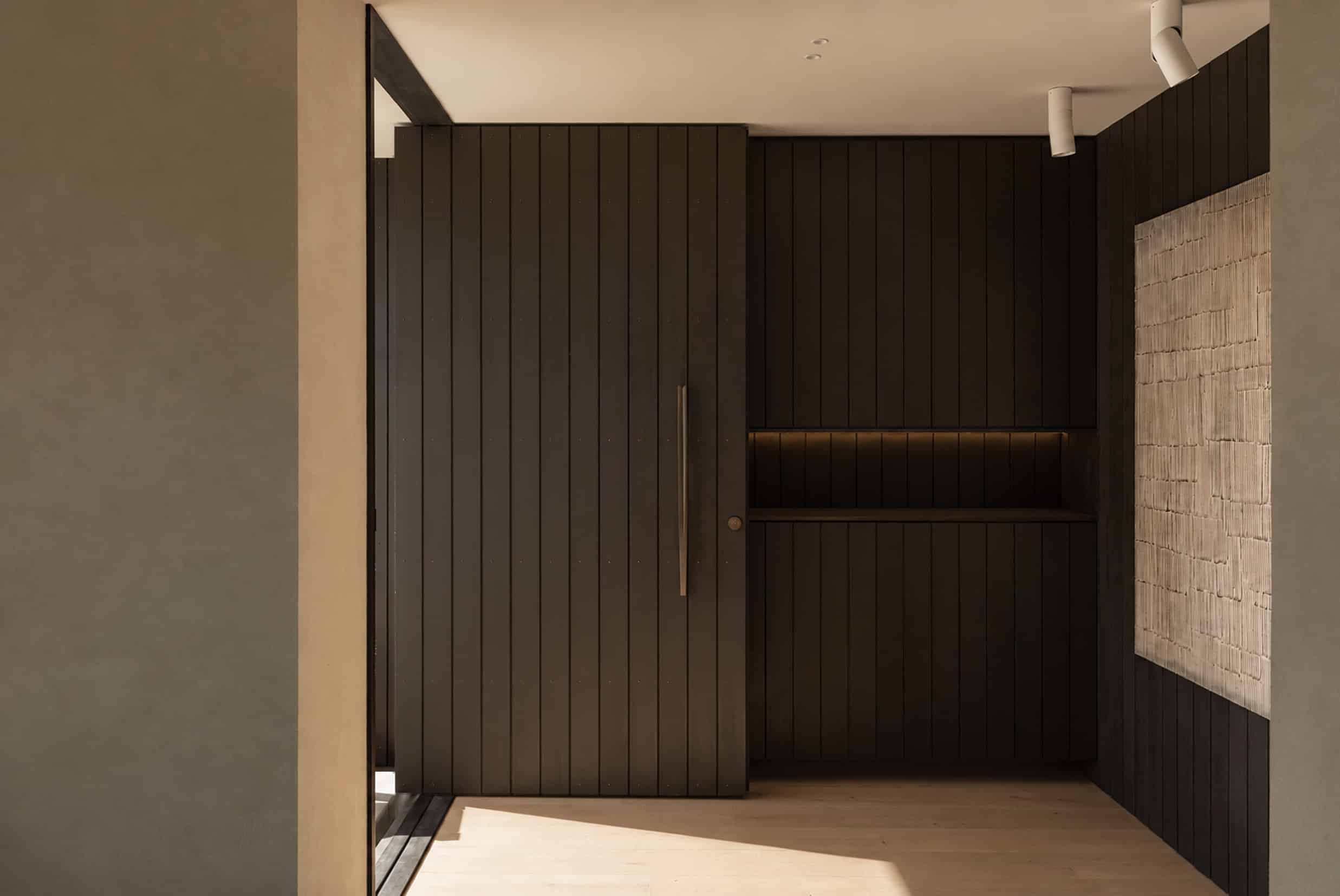 Icons Conde oak flooring at the entry of a Hobsonville home, beside a tall dark board-clad timber pivot door.
