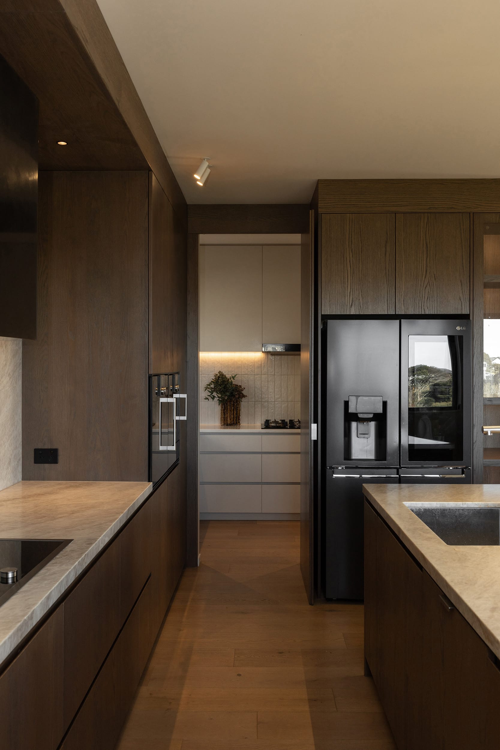 Icons Conde oak flooring in a Hobsonville kitchen, framed by dark stained oak cabinetry and stone benchtops.