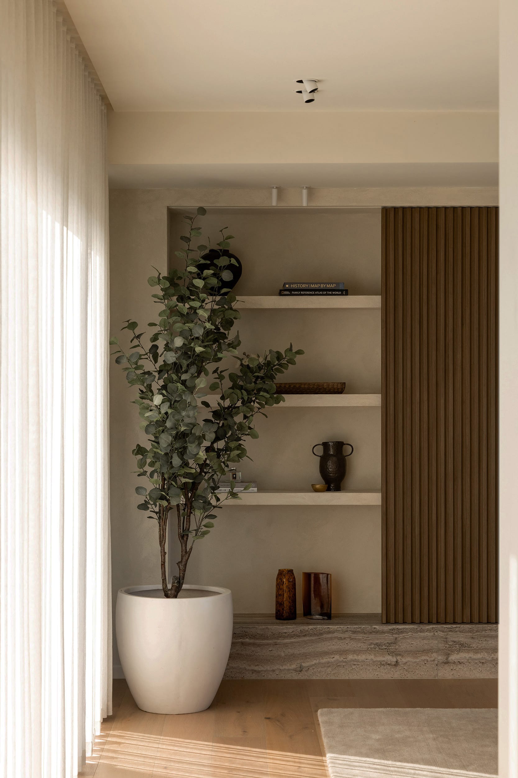 Icons Conde oak flooring in a quiet nook, with plaster shelving, a potted tree and the edge of a fluted timber wall.