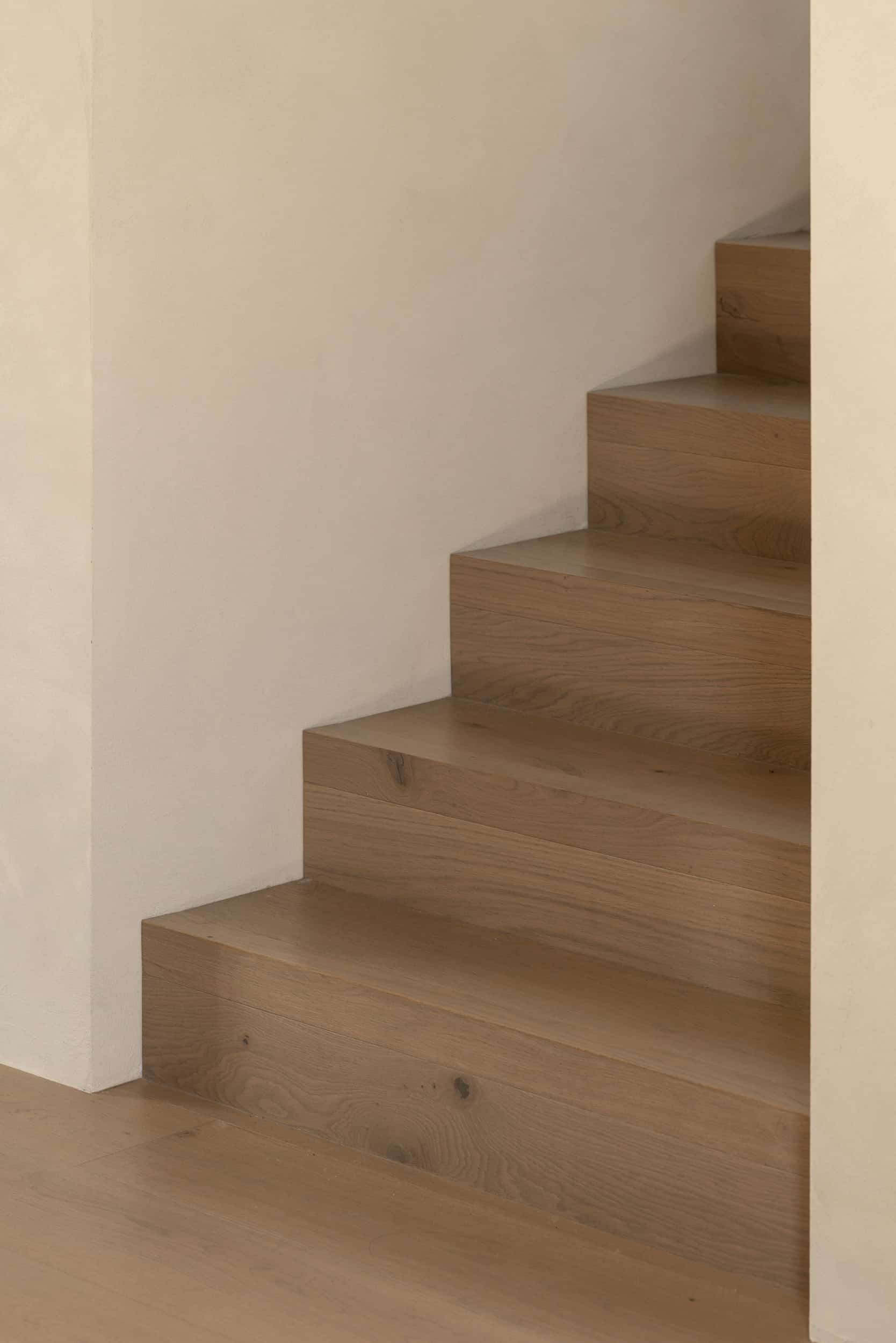 Detail of oak stair treads meeting the Conde floor against a plaster wall, showing the grain and the knots.