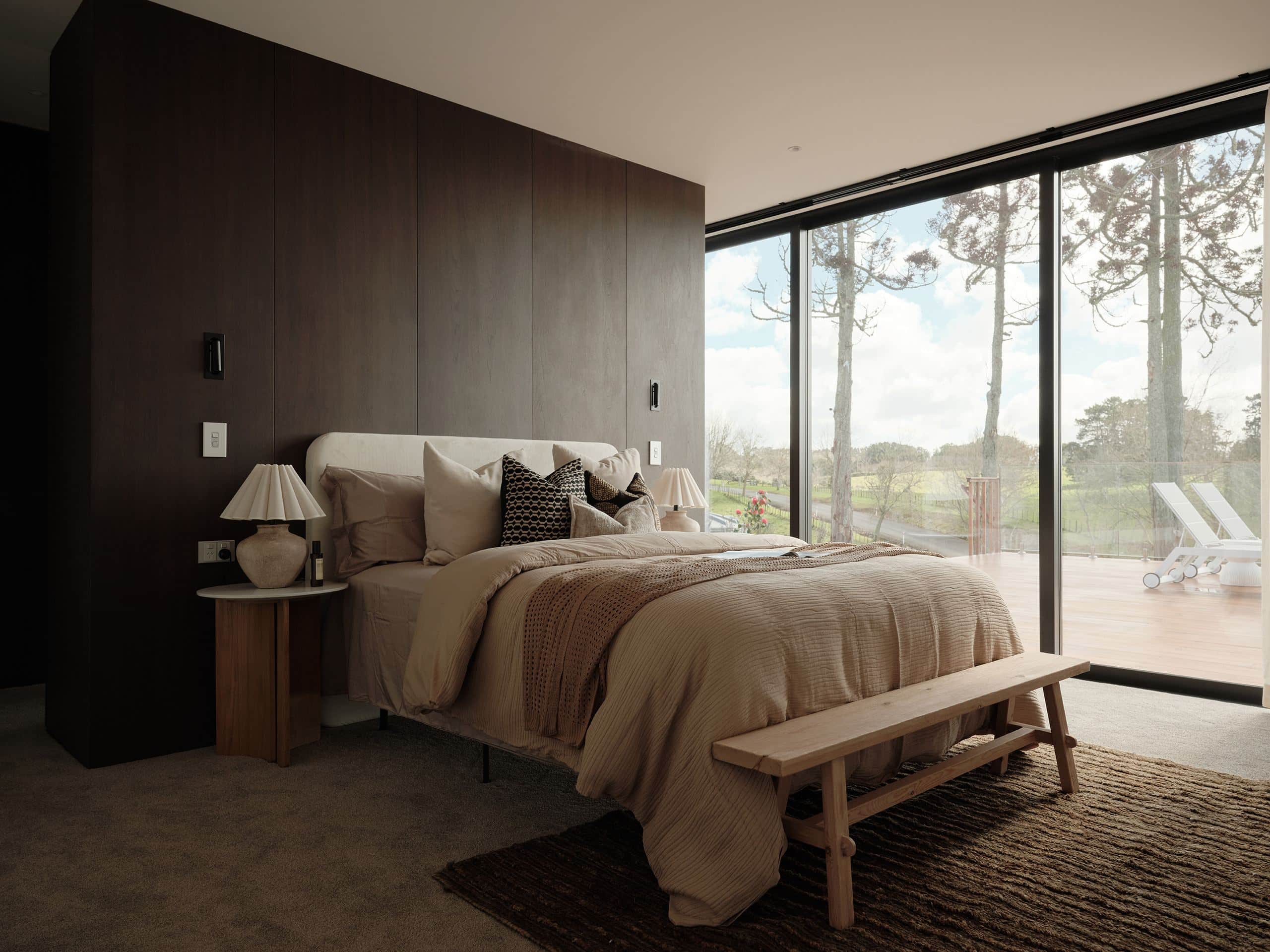 A bedroom in a Taupaki home, with full-height glazing onto a deck and open farmland beyond.