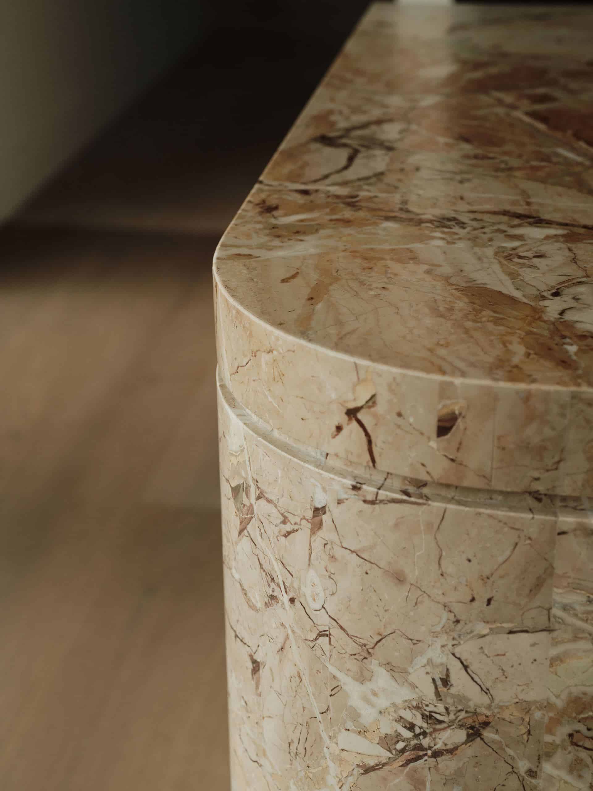 Detail of a rounded, veined-stone kitchen island in a Taupaki home, with timber flooring out of focus behind it.